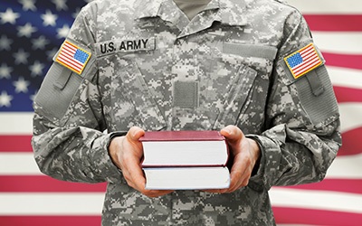 US Army military member in uniform holding textbooks standing in front of an American Flag