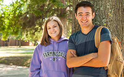 Two smiling college students by a tree on campus.