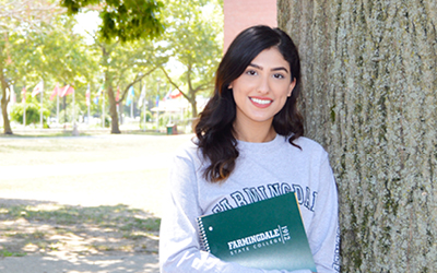 Female student leaning against a tree holding a FSC notebook.