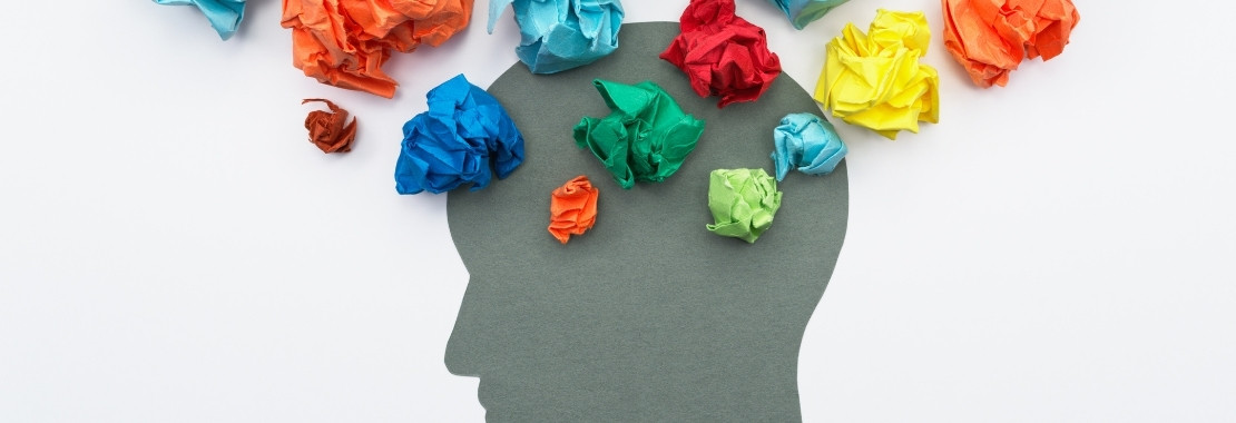 Paper head silhouette surrounded by crumpled pieces of multicolored paper of varying sizes