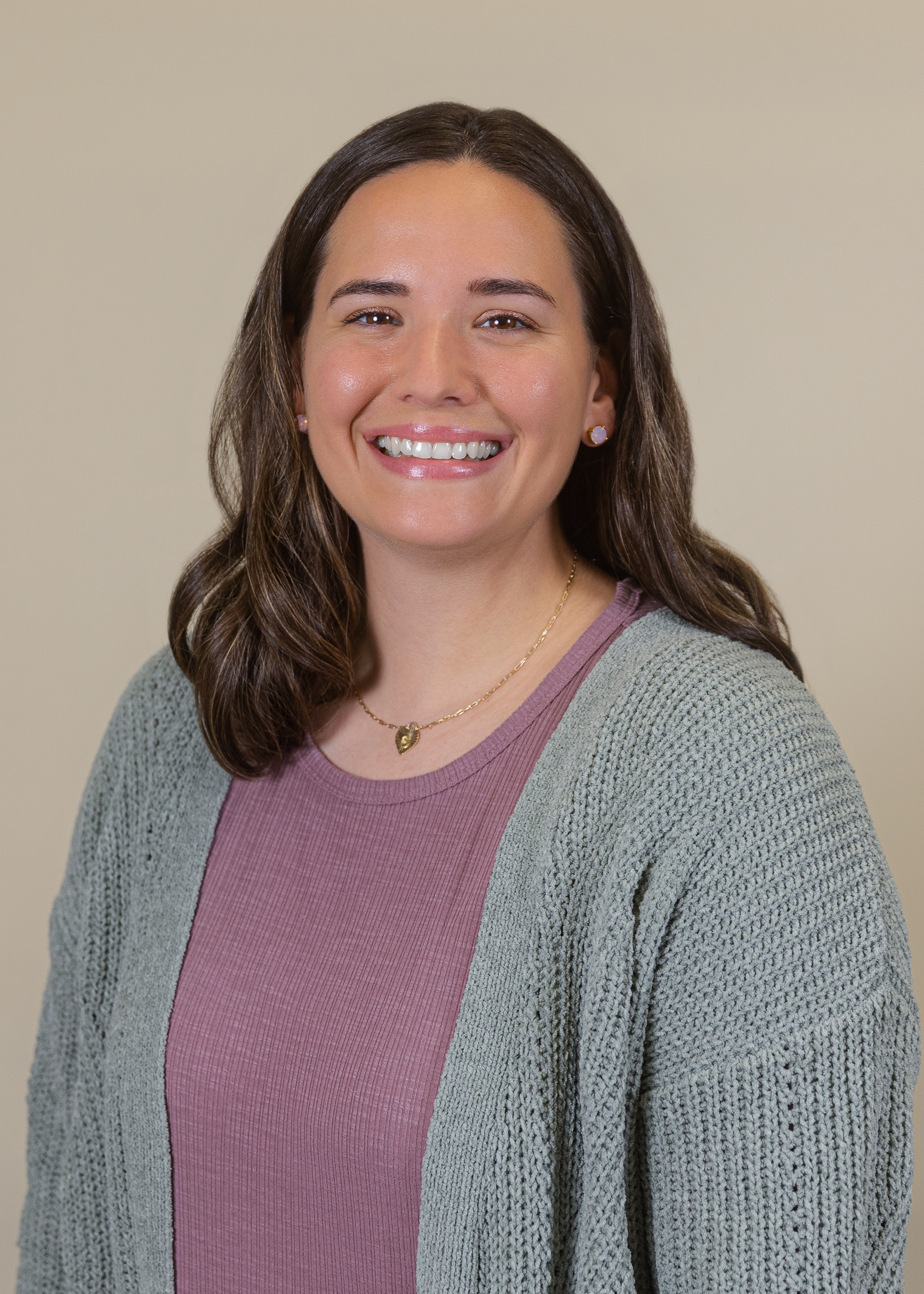 caucasian woman wearing a pink shirt and grey cardigan smiling